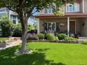 Beautifully landscaped front yard featuring lush green grass, trees, and well-maintained flower beds leading to the covered porch at 4907 Fenwood Dr, Highlands Ranch, CO 80130