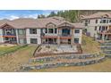 Two-story home with balconies, a patio, tiered stone landscaping, and iron fencing at 1015 Nob Hill Rd, Evergreen, CO 80439