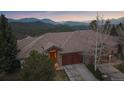 Beautiful exterior view of a stone home with a wooden garage door nestled amongst the mountains at dusk at 1015 Nob Hill Rd, Evergreen, CO 80439