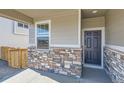 Covered front porch area with a gray front door and stone detailing on the home's exterior at 17467 E 89Th Way, Commerce City, CO 80022