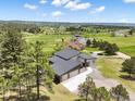 An elevated view showcasing the modern home surrounded by lush greenery and expansive rural fields with mountain views at 3630 Mesa Verde Rd, Monument, CO 80132