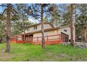 Side view of a tan home with a large wraparound deck and an attached garage at 28735 Little Big Horn Dr, Evergreen, CO 80439