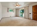 Bright living room features neutral carpet, white walls, large window, ceiling fan, and a wooden front door at 1803 Graves Ct, Northglenn, CO 80233