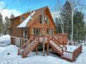 Beautiful view of log cabin with a spacious wooden deck, chimney, and stairs surrounded by mature trees in winter at 11498 Pauls Ln, Conifer, CO 80433