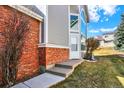 Close up on brick accents and a front door entrance with gray siding under a partly cloudy, bright blue sky at 7707 S Monaco Cir, Centennial, CO 80112