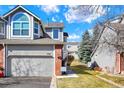 Shot of a two-story townhome featuring an attached garage, gray siding and brick accents under a bright blue sky at 7707 S Monaco Cir, Centennial, CO 80112