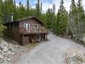 Exterior view of a two-story cabin in a forest with a large deck and gravel driveway at 159 Lake Rd, Idaho Springs, CO 80452