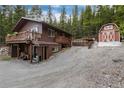 Cozy two-story cabin with a deck and red barn surrounded by a lush forest and a gravel driveway at 159 Lake Rd, Idaho Springs, CO 80452