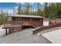 Exterior two-story cabin with a deck and garage nestled in a wooded area with a gravel driveway at 159 Lake Rd, Idaho Springs, CO 80452