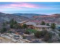 Panoramic view of home nestled in foothills, boasting natural stone and tile roof against the colors of the mountain sunset at 15175 W Belleview Ave, Morrison, CO 80465
