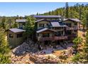 Exterior features multi-tiered decks and stone patio with fire pit, surrounded by lush trees and rocky landscape at 3395 Timbergate Trl, Evergreen, CO 80439