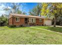 Inviting single-story brick home with a lush green lawn, mature tree, and attached garage at 8660 De Soto St, Denver, CO 80229