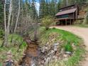 Charming creek-side view of a two-story home surrounded by a forest at 28272 Shadow Mountain Dr, Conifer, CO 80433