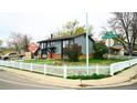 Corner lot home with gray siding, a red door, white picket fence, and mature landscaping enhancing curb appeal at 1528 Coronado Pkwy, Denver, CO 80229