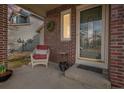 Cozy front porch with brick columns is adorned with an outdoor chair, flowers, and decorative wreath at 11613 W Coal Mine Dr, Littleton, CO 80127