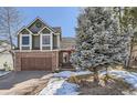 Charming two-story home featuring a brick and wood exterior, complemented by a paved driveway and mature landscaping at 27 Buckthorn Dr, Littleton, CO 80127