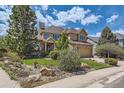 Tan and stone two-story home showcasing a lush lawn and mature trees at 7083 Turweston Ln, Castle Pines, CO 80108
