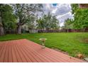 Expansive backyard featuring lush green grass, mature trees, and a wooden deck with small bird bath at 1705 Stonehenge Dr, Lafayette, CO 80026