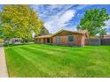 Brick home with a large, lush front lawn featuring mature trees, blue skies, and a quiet residential street at 2311 Emery Pl, Longmont, CO 80501