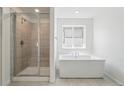 Modern bathroom with a glass-enclosed shower, freestanding soaking tub, bright window, and neutral tile flooring at 7291 Prairie Sage Pl, Littleton, CO 80125