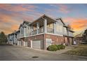 Charming townhome showcasing a brick facade, private garages, and second-story balcony with sunset sky backdrop at 74 Whitehaven Cir, Highlands Ranch, CO 80129