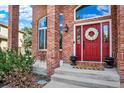 Inviting front porch features a red door adorned with a wreath, framed by brick pillars and manicured landscaping at 7271 Brixham Cir, Castle Pines, CO 80108