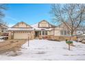 Beige two-story house with stone accents, a three-car garage, and a snow-covered yard at 23405 E Elmhurst Pl, Aurora, CO 80016