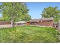 A large, grassy backyard with mature trees, wooden fences, and a brick home in the background at 921 Dakin St, Denver, CO 80221