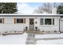 Charming single-story home featuring white brick, a gray door and shutters and a snow-covered front yard at 13438 W 23Rd Pl, Golden, CO 80401