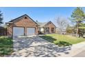 View of a brick home with a well-manicured lawn and a two-car garage at 6991 S Lee Way, Littleton, CO 80127