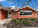 Close-up of the front of the brick home with a large window and well-maintained landscaping at 7105 Dover Way, Arvada, CO 80004