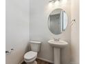 Small half bathroom with pedestal sink, toilet, and round mirror at 9663 Ceylon St, Commerce City, CO 80022