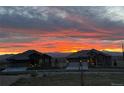 Stunning sunset view of two homes in the distance with a vibrant orange and yellow sky and mountain backdrop at 15637 Deer Mountain Cir, Broomfield, CO 80023