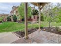 Inviting covered patio with stone flooring, wood posts, and a hanging flower basket, overlooking the lawn and community at 9592 Firenze Way, Highlands Ranch, CO 80126