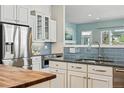 Modern kitchen with stainless steel appliances, blue subway tile backsplash, white cabinetry, and a butcher block countertop at 6273 Torrey Ln, Arvada, CO 80403