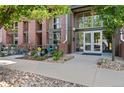 The Lofts at Central Park: Entrance to 7700 building with brick facade, green landscaping, and sidewalk in front at 7700 E 29 Ave # 304, Denver, CO 80238