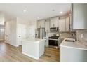 Modern kitchen features an island, stainless steel appliances, light gray cabinetry, and attractive wood-look floors at 9484 Yampa St, Commerce City, CO 80022