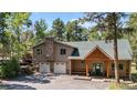 Charming two-story home features a stone chimney, a front porch with a wooden structure, and a well-maintained yard at 26196 Rea Ave, Conifer, CO 80433