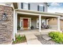 Inviting covered front porch with a porch swing, stone accents, and a vibrant red front door at 12000 Horseshoe Ln, Parker, CO 80138