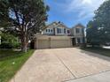 Traditional home featuring a three car garage, mature trees, and a large driveway with a sidewalk at 17130 Opal Hill Dr, Parker, CO 80134