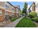 Exterior view of a townhome with stone accents and neutral siding, surrounded by lush greenery and a sidewalk at 4385 S Balsam St # 3-101, Littleton, CO 80123