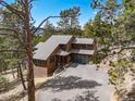 Aerial view of a two-story house featuring a well-manicured lawn and mature trees in a mountain community at 7395 Heiter Hill Dr, Evergreen, CO 80439