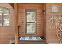 Close-up of the front door with a storm door, wood siding, and small decorative window at 7395 Heiter Hill Dr, Evergreen, CO 80439