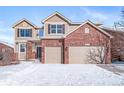 Two-story house with brick and siding, two-car garage, snow-covered yard at 19427 Dunraven St, Parker, CO 80134