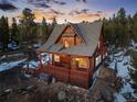 A wooded two-story home with a sloped roof, full deck, mature trees, and unique mountain charm at dusk at 439 Ronnie Rd, Golden, CO 80403