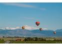 Scenic view of colorful hot air balloons floating over a lush green landscape with snow-capped mountains at 651 Sunrise St, Erie, CO 80516