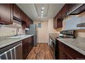 Galley kitchen featuring stainless steel appliances, granite countertops, dark wood cabinets and wood-look floors at 13393 E Asbury Dr # 103, Aurora, CO 80014