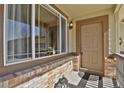 A home's front porch featuring brick accents, a large window, and a tan front door with a black mat at 24269 E Arapahoe Pl, Aurora, CO 80016