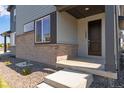 Close-up of a home's entry showing brick foundation and covered porch with a dark front door and concrete steps at 1443 Great Western Dr, Longmont, CO 80501