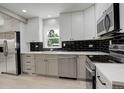 Bright kitchen featuring stainless steel appliances, white cabinets, and black backsplash at 1925 Syracuse St, Denver, CO 80220